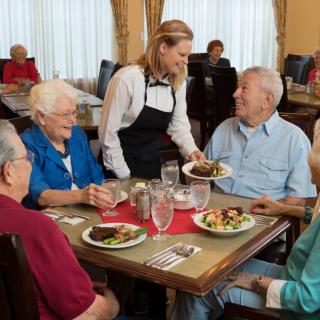 A group of seniors dining at a restaurant, served by a waitress.