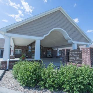 An entrance to a brick and siding building with landscaped greenery under a clear blue sky.