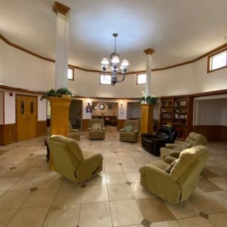 A spacious lobby with armchairs arranged in a circle, complemented by a chandelier and bookshelves.