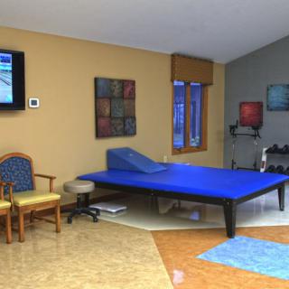 A well-equipped physical therapy room with a therapy bed, exercise equipment, and chairs.