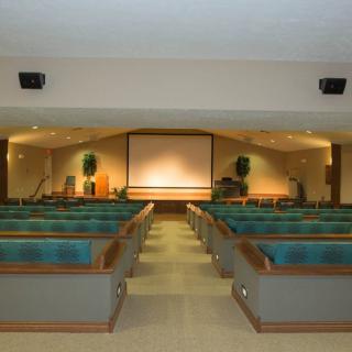 An empty auditorium with rows of seats facing a projection screen and stage.
