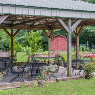 A wooden gazebo with tables and chairs surrounded by lush greenery.