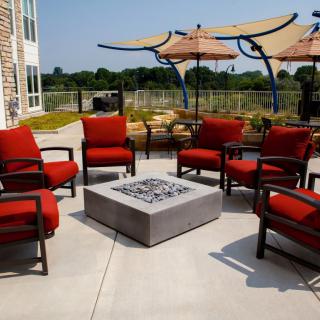 A cozy outdoor patio setup with red cushioned chairs surrounding a fire pit under large umbrellas.