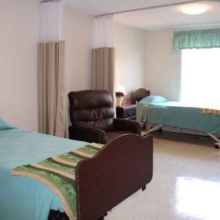 A cozy nursing home room with two beds, chairs, and a large window.