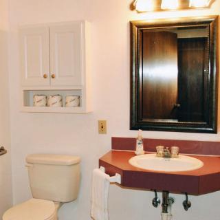 A bathroom with a red countertop, sink, mirror, and wall-mounted shelves.