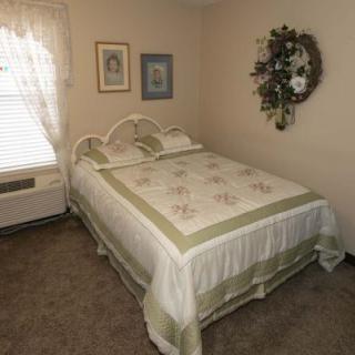 A cozy bedroom featuring a neatly made bed with a decorative quilt, adorned with wall art and curtains.