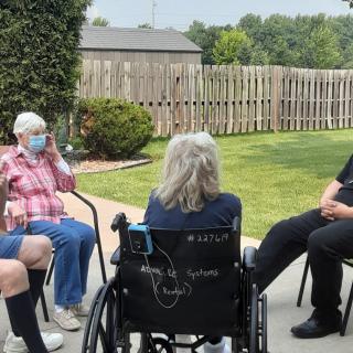 A group of people having a conversation in a garden setting, with one person in a wheelchair.
