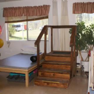 A room with wooden stairs, a table, and large windows with curtains.