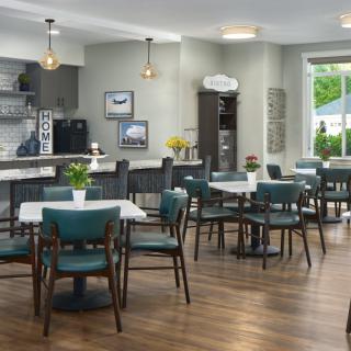 A modern cafe interior with wooden floors, teal chairs, and ample natural light.