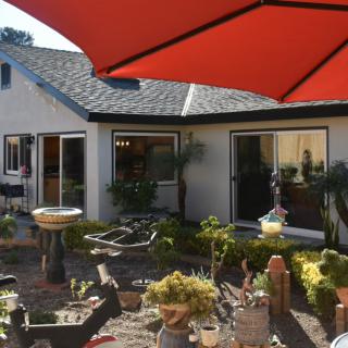 A sunny backyard garden with a patio and red umbrella.