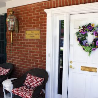 A welcoming entrance featuring a decorative wreath, cozy seating, and a charming brick facade.