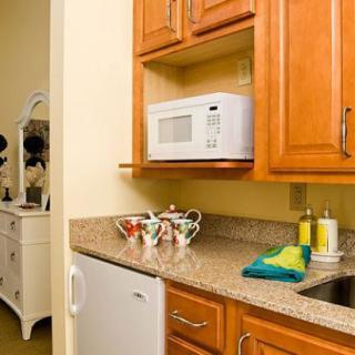 A cozy kitchen corner featuring a microwave within wooden cabinets, a small fridge, and teacups on the countertop.