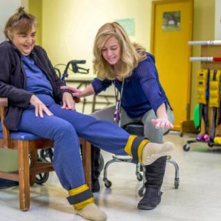 A physical therapist assists an elderly woman with leg exercises in a rehabilitation center.
