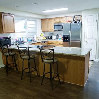 A modern kitchen with wooden cabinets, a large countertop with bar stools, and stainless steel appliances.