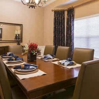 A neatly set dining room table with elegant place settings and a chandelier overhead.