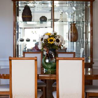 A modern dining room setup featuring a wooden table, upholstered chairs, and a glass display cabinet adorned with decorative items and a vibrant floral arrangement.