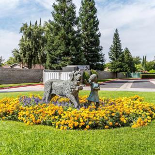 A sculpture of a child with a lamb surrounded by vibrant yellow flowers in a landscaped garden.