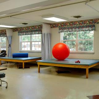 A spacious rehabilitation therapy room featuring a red exercise ball and therapy tables, designed for physical recovery.