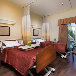 A well-lit hospital room featuring two patient beds with bedside tables and curtains, providing a comfortable healthcare environment.