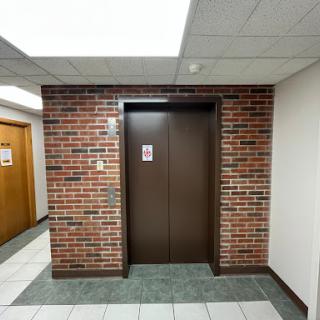 An elevator entrance located between brick and tiled walls in a building hallway.