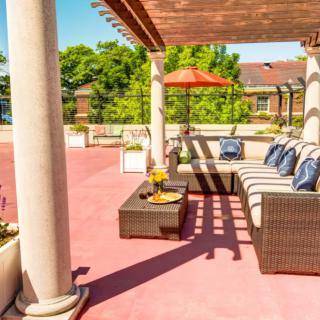 A sunny patio with comfortable outdoor seating under a pergola, featuring cozy cushions and a vibrant umbrella.