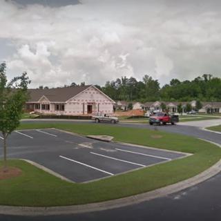 A small building with a parking lot, surrounded by trees under a cloudy sky.
