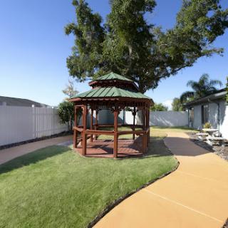 A serene outdoor garden featuring a wooden gazebo surrounded by lush grass and a winding pathway.
