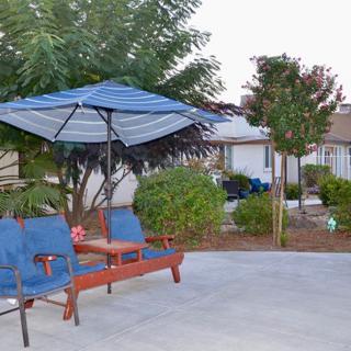 A cozy backyard patio with a blue umbrella and outdoor seating surrounded by greenery.