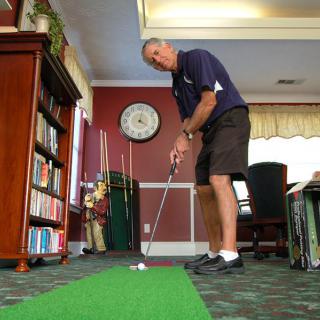 A person practicing their putting skills indoors on a green carpet.