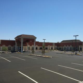 A commercial building with an empty parking lot under a clear blue sky.