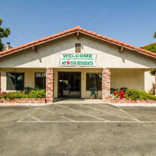 A small storefront with a welcoming sign, featuring a parking area in front.