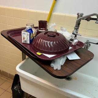 A piled-up tray with food containers balanced on a sink, illustrating a cluttered kitchen space.