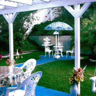 A picturesque garden setup with tables, chairs, and a decorative umbrella amidst lush greenery.