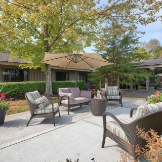 A cozy outdoor patio area with comfortable seating and a large umbrella, surrounded by lush greenery.