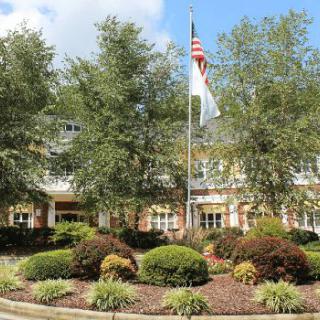 A well-maintained building surrounded by landscaped gardens and trees, with flags flying on a sunny day.