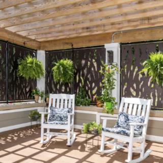 A cozy outdoor patio featuring two white rocking chairs surrounded by lush greenery.
