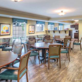 A bright and spacious dining area with wood flooring, featuring multiple tables and chairs, decorated with artwork on the walls and illuminated by ceiling lights.