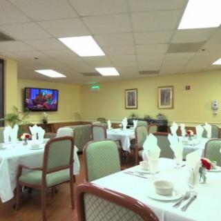 A formal dining room with neatly arranged tables and chairs, set for a meal. A television is mounted on the wall.