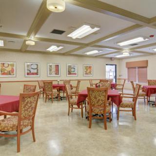 A spacious dining area featuring tables with red tablecloths and decorative chairs, complemented by artwork on the walls.