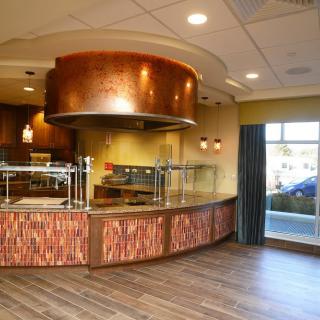 A modern restaurant interior featuring a sleek counter with a copper finish and ample natural light.