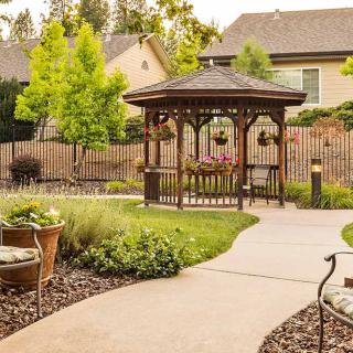 A picturesque garden featuring a wooden gazebo surrounded by lush greenery and a winding pathway.