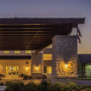 A well-lit building entrance during the evening, featuring stone pillars and modern architecture.