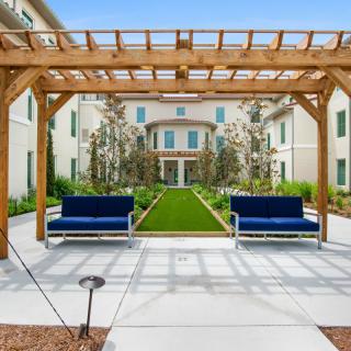 A well-designed courtyard featuring a pergola with blue benches and lush landscaping in front of an elegant building.