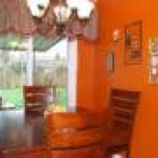 A vibrant dining room with orange walls, featuring a large window and a chandelier.