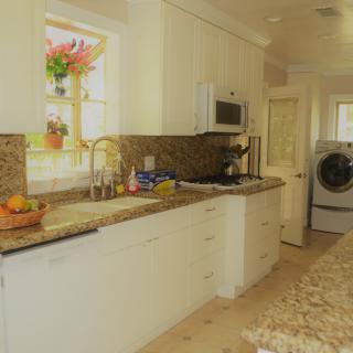 A bright kitchen interior with white cabinets, granite countertops, and a view of an adjacent laundry area.