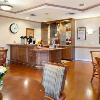 A cozy dining area with a coffee station, featuring wooden tables and chairs on a hardwood floor.