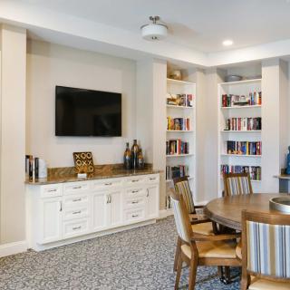 A cozy living room with built-in bookshelves, a mounted TV, and a dining table with chairs.