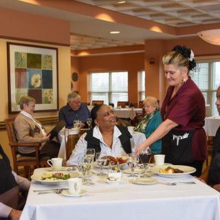 A waitress serves a group of elderly individuals enjoying a meal at a restaurant.