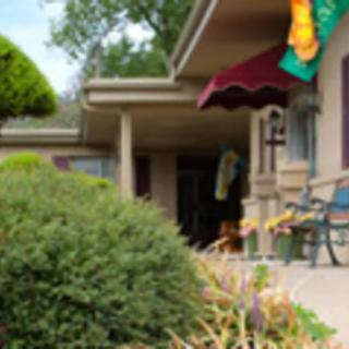A small house with a front porch, surrounded by greenery and an awning.