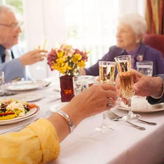 Elderly individuals enjoying a celebratory meal with a toast at a formal dining table.